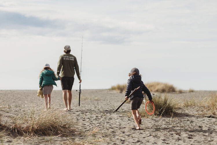 An adult and two children walk on a beach holding fishing poles.
