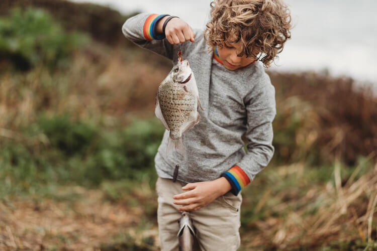A child holds two fish on a fishing line.