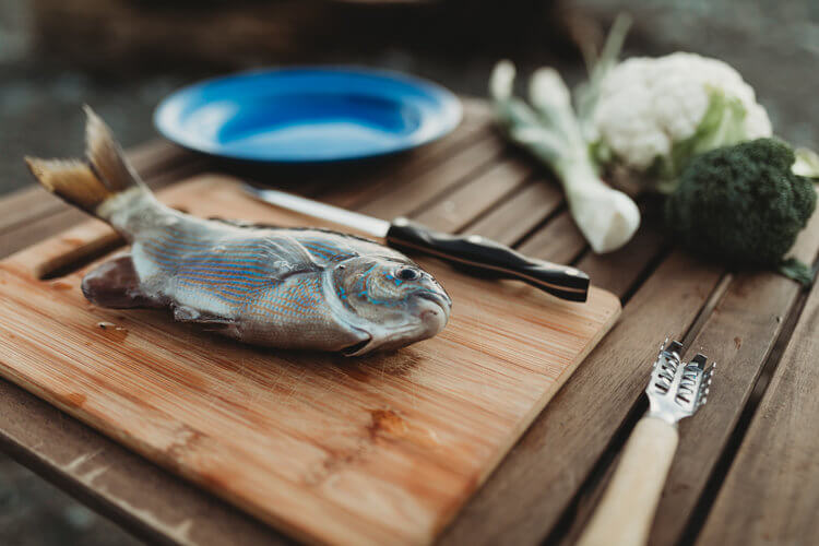 Surf perch fish on a cutting board with vegetables in the background.  