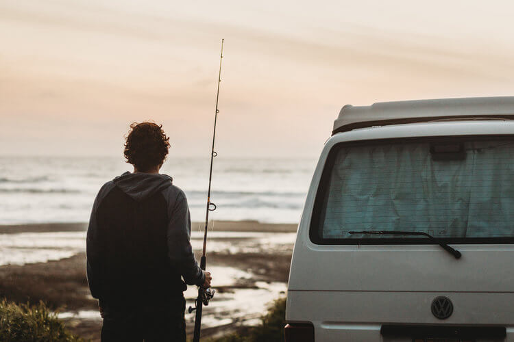 Man with fishing pole next to a Volkswagen Eurovan Camper at the coast.