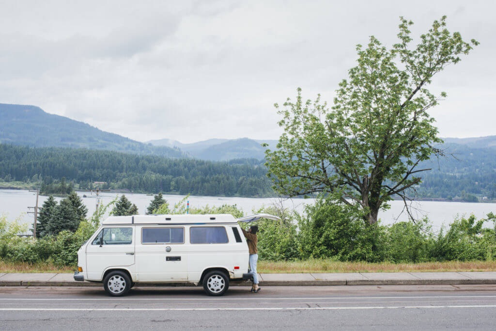 Woman access back hatch of a Volkswagen Vanagon Camper while on the highway in the Columbia River Gorge. 