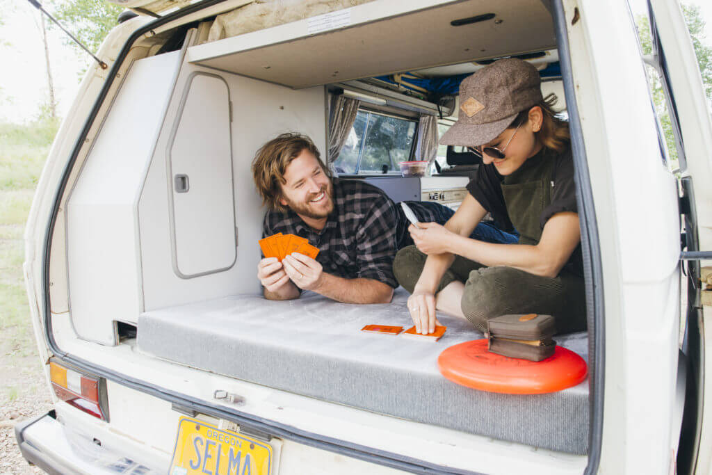 Couple plays cards in the back of a Volkswagen Vanagon Camper with the rear door open