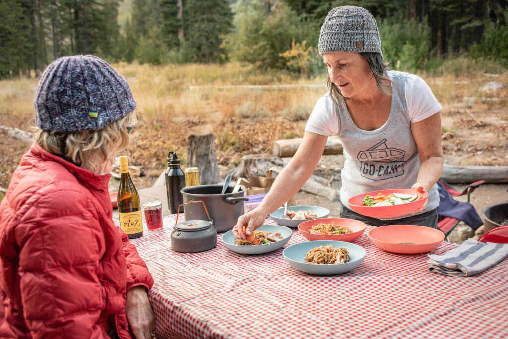 Woman serves ramen noodle bowls in a campground.