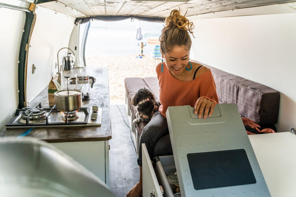 Woman with a dog in the back of camper van looking into the cooler